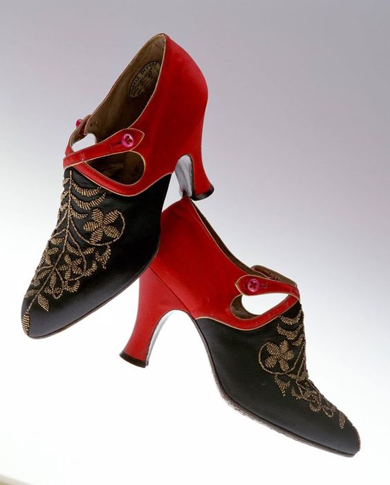 Une paire de talons hauts rouges et noirs. Le dessus de la chaussure est orné d\\\'un motif en or.